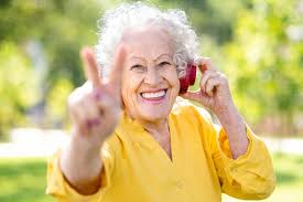 elderly woman in yellow holding up a peace sign while listening to music with red headphones